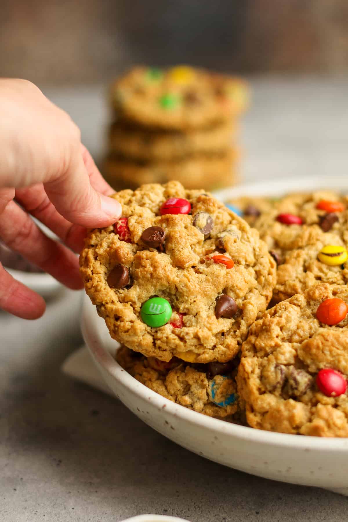 A hand reaching for a flourless monster cookie from a bowl of cookies.