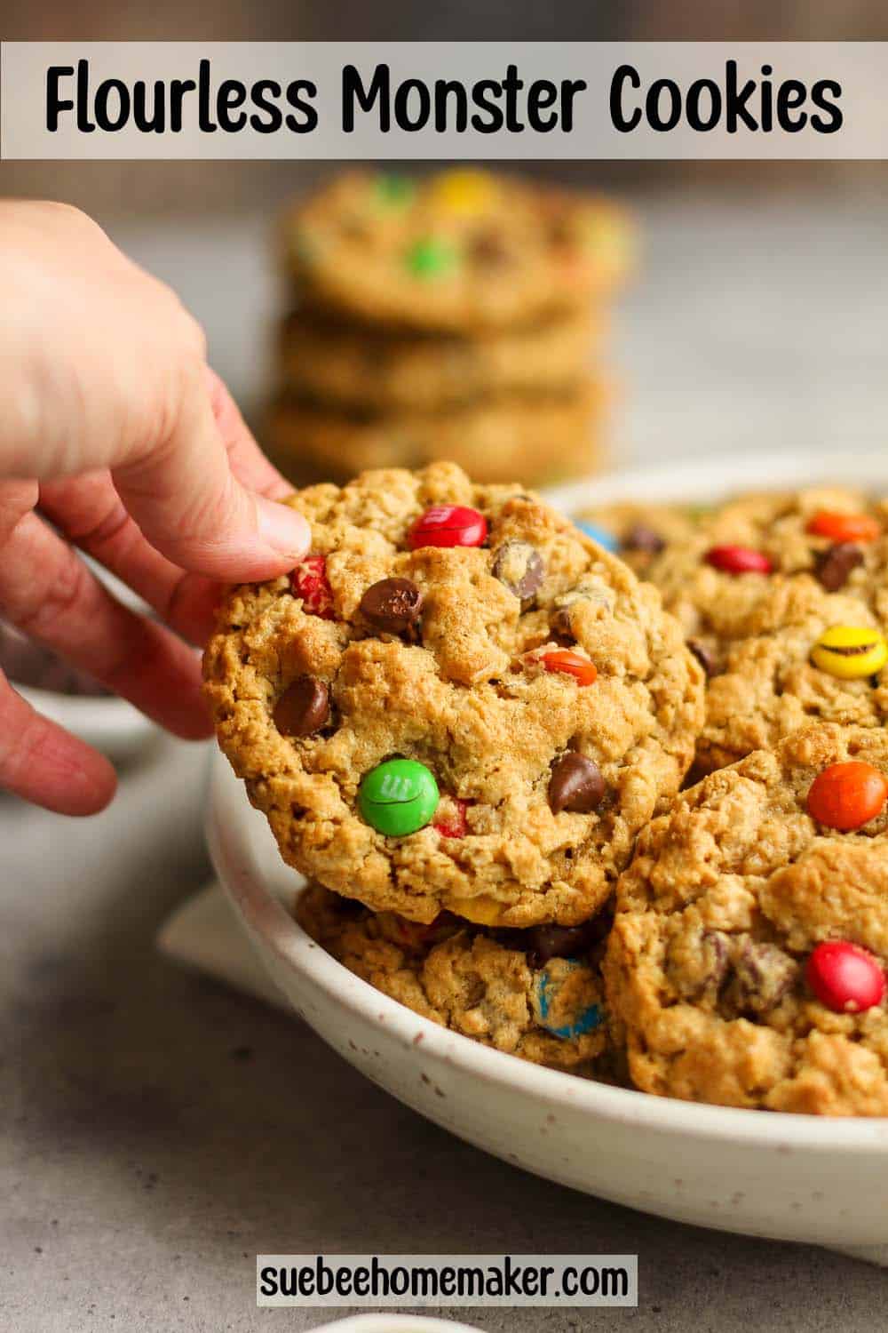 A bowl of flourless monster cookies with m&ms and a hand reaching for one.