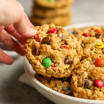 A hand reaching for a flourless monster cookie from a bowl.