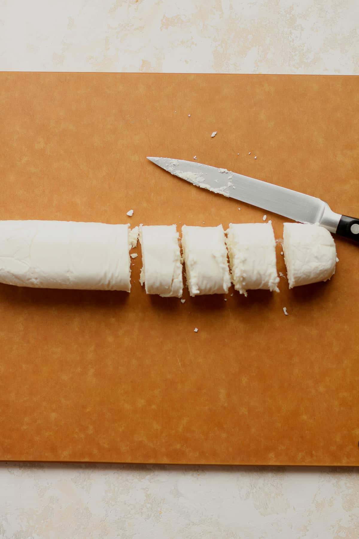A board with a log of goat cheese, some sliced, and a knife beside it.