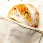 A loaf of jalapeno cheddar sourdough bread in a linen bag.