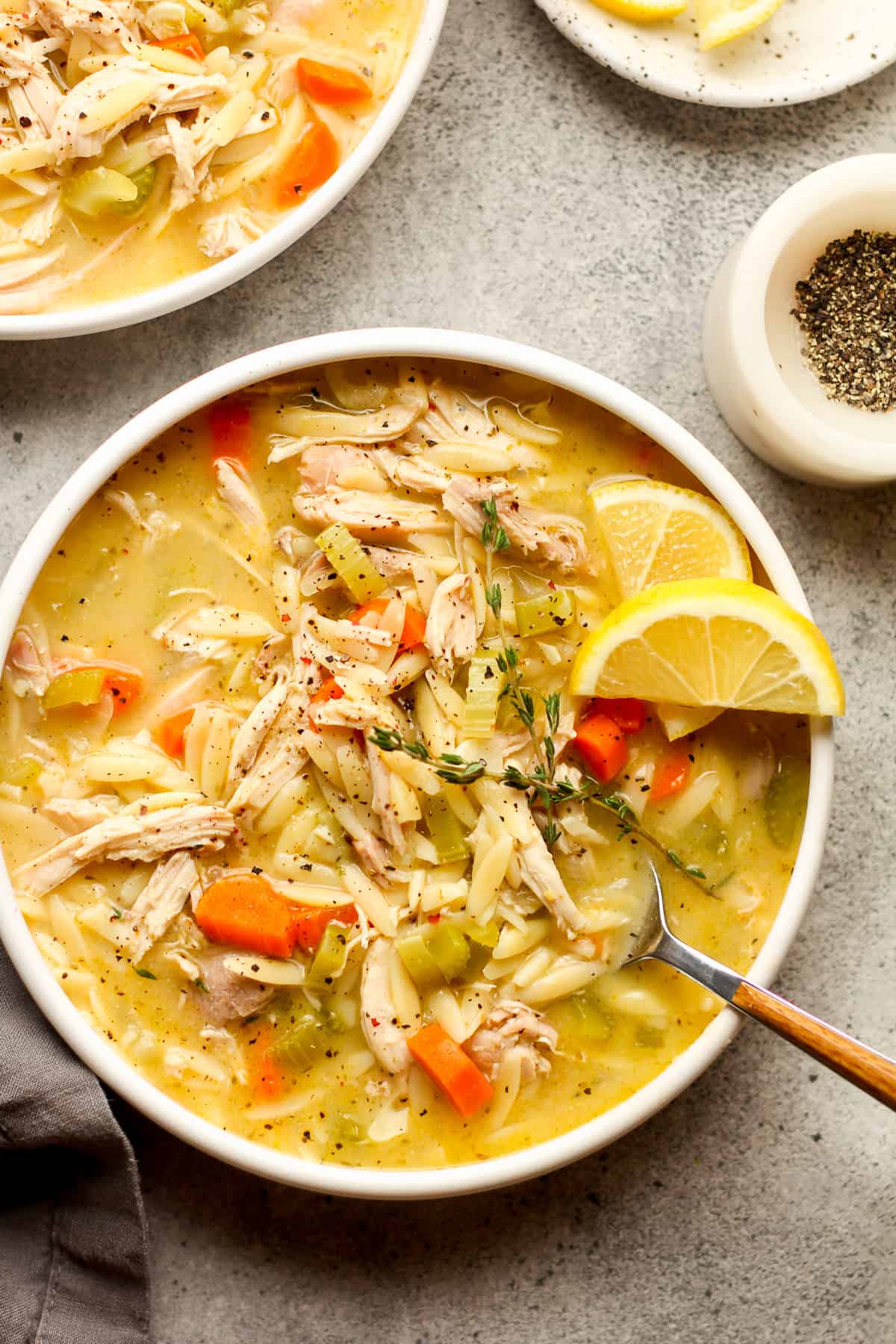 A bowl of lemon orzo soup with chicken on a gray background.