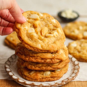 A hand reaching for a cookie on a stack of cookies.