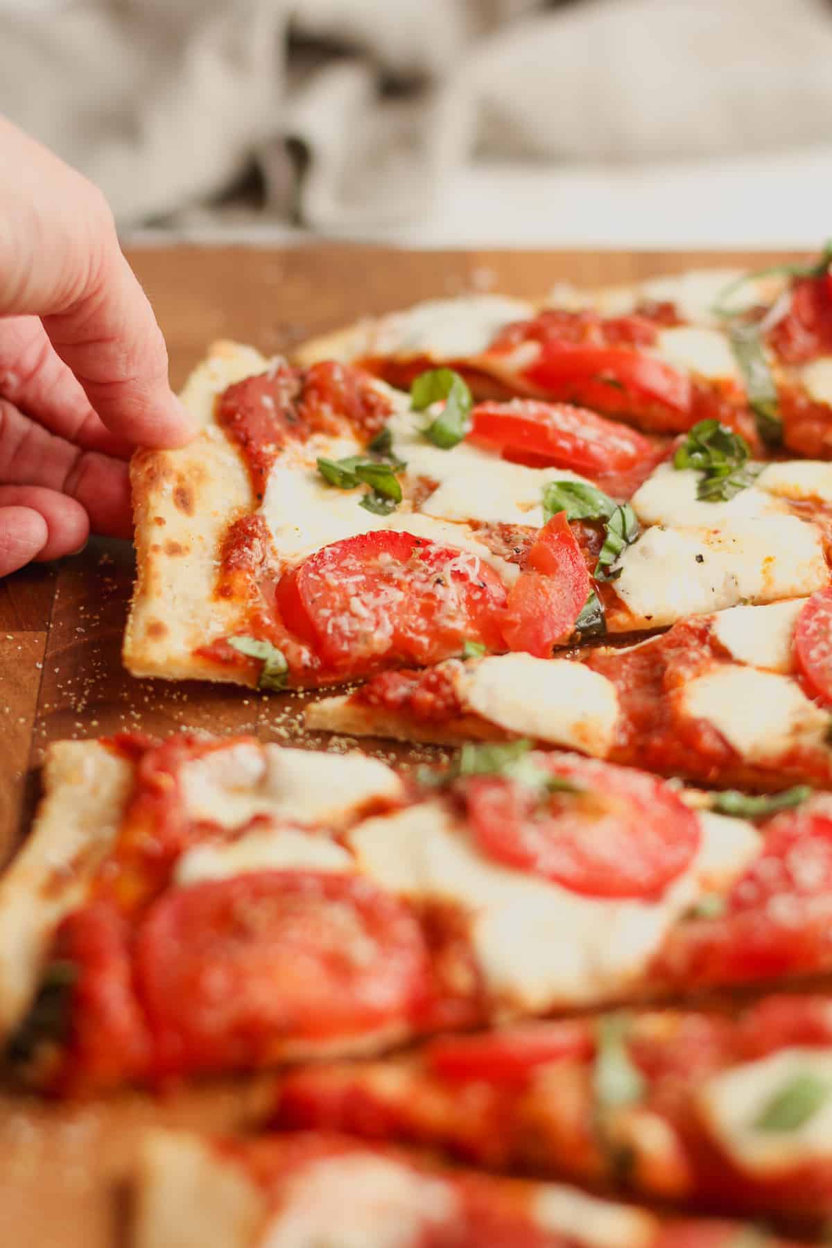A hand reaching for a slice of Margherita flatbread pizza.