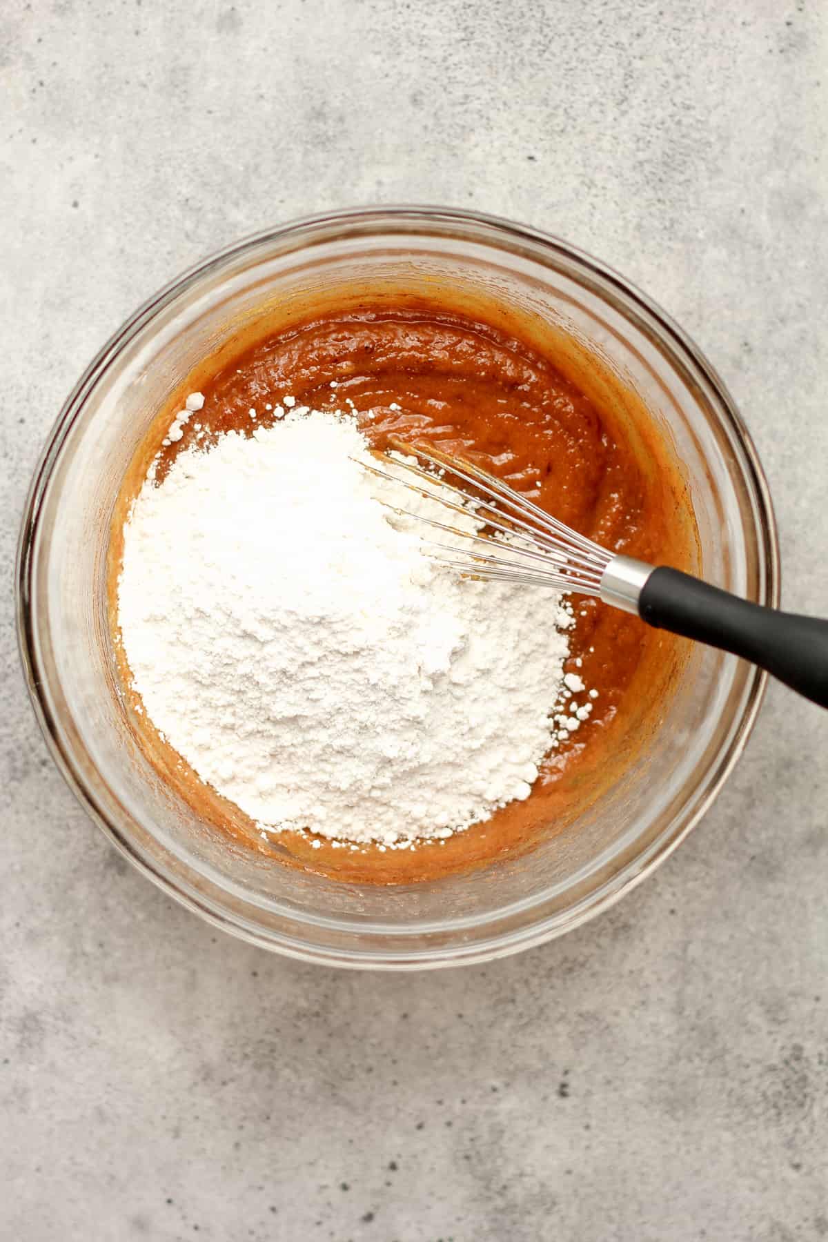 A bowl of the wet ingredients with the flour on top with a whisk.