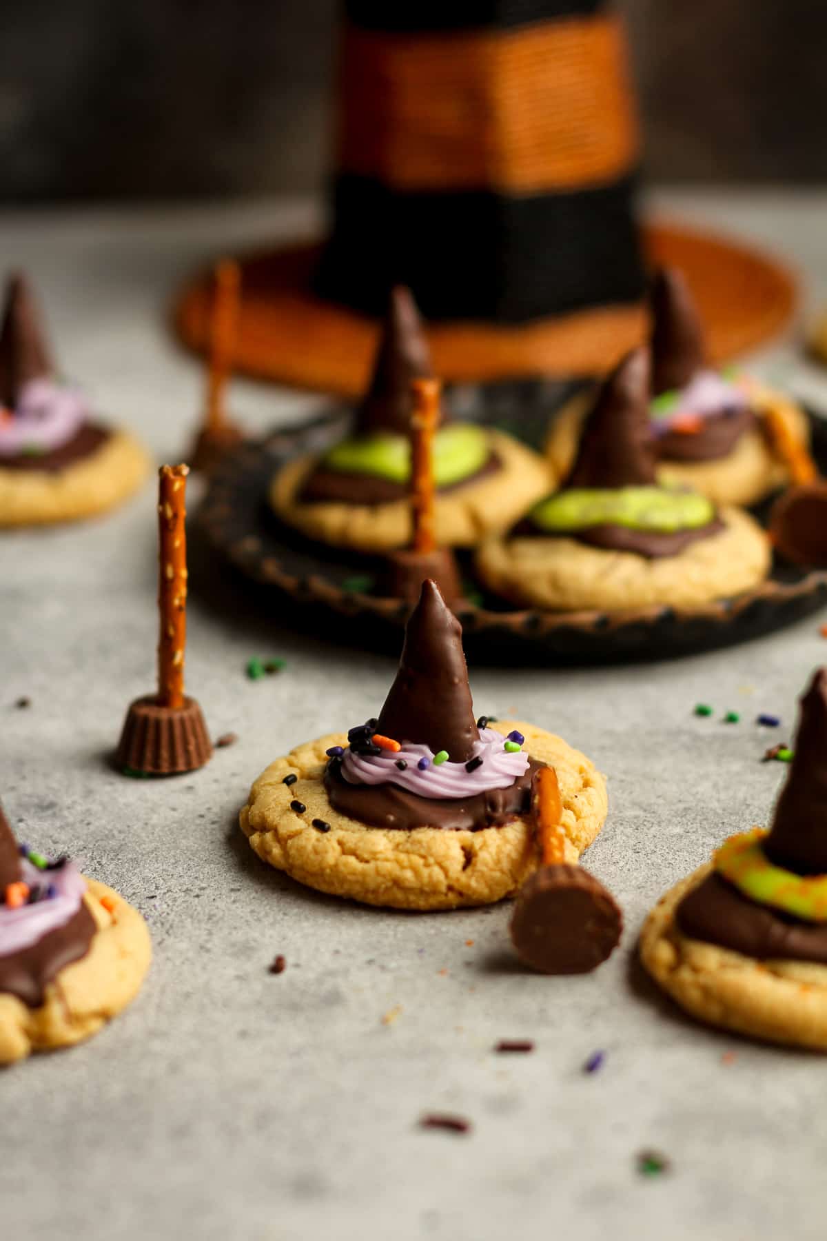 Side view of a peanut butter witch hat cookie with broomsticks beside it.