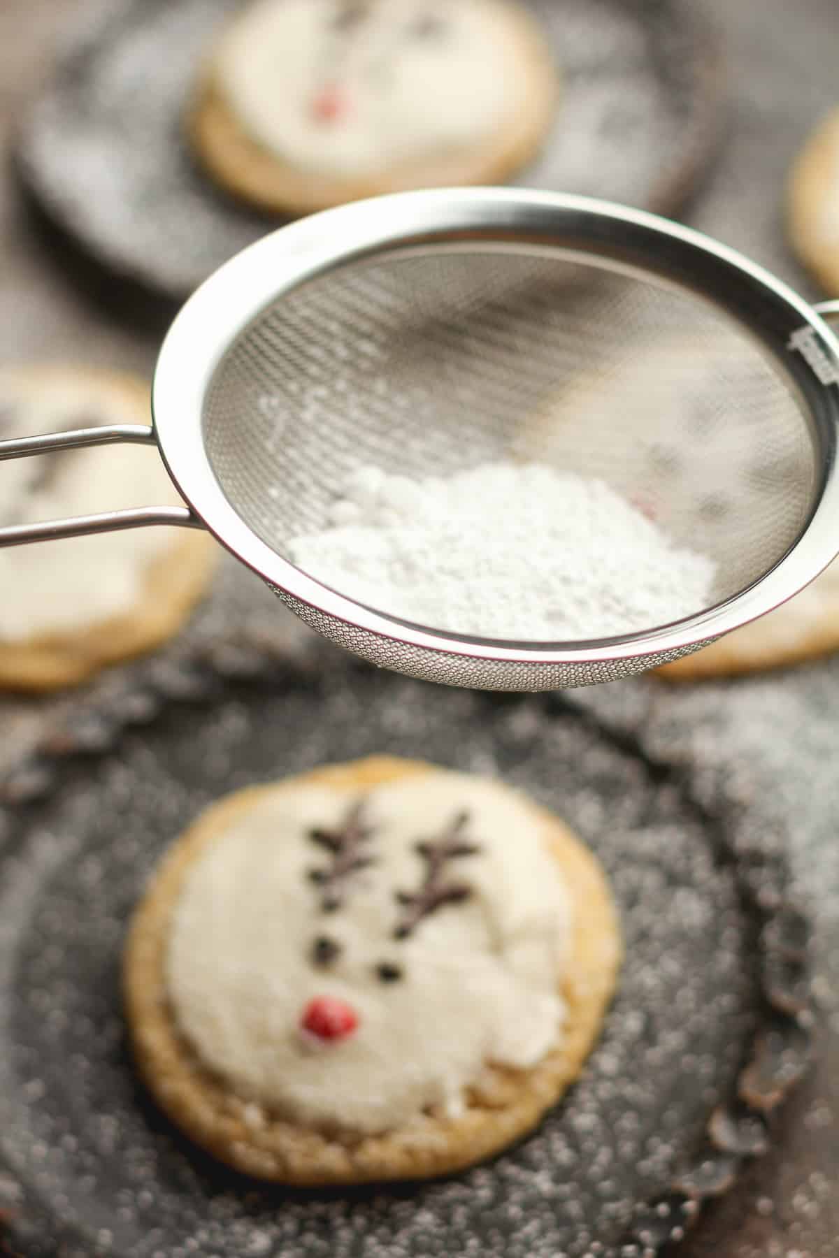 A small thing of powdered sugar over a plate with a reindeer cookie.