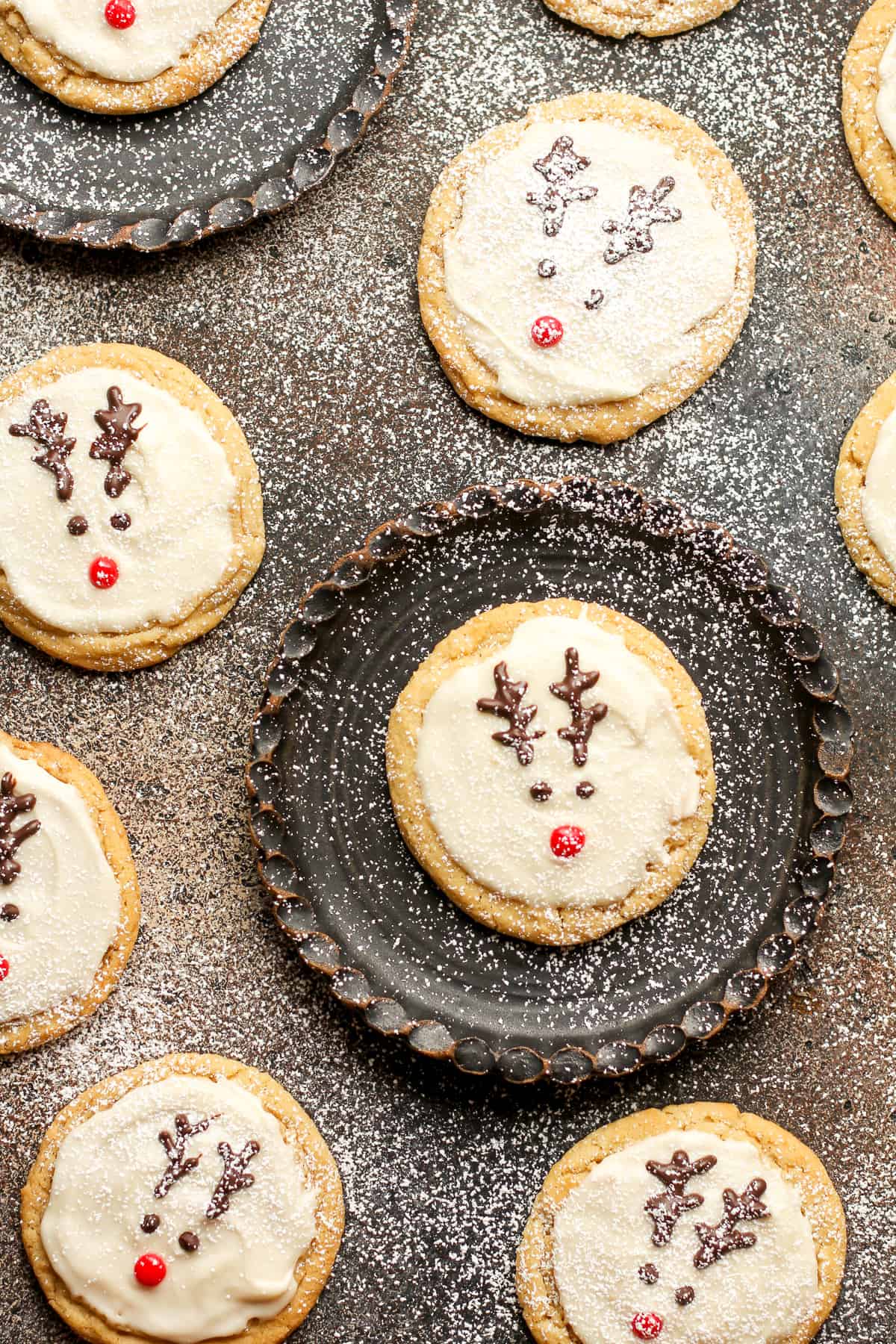 Overhead shot of several reindeer sugar cookies on a black surface.