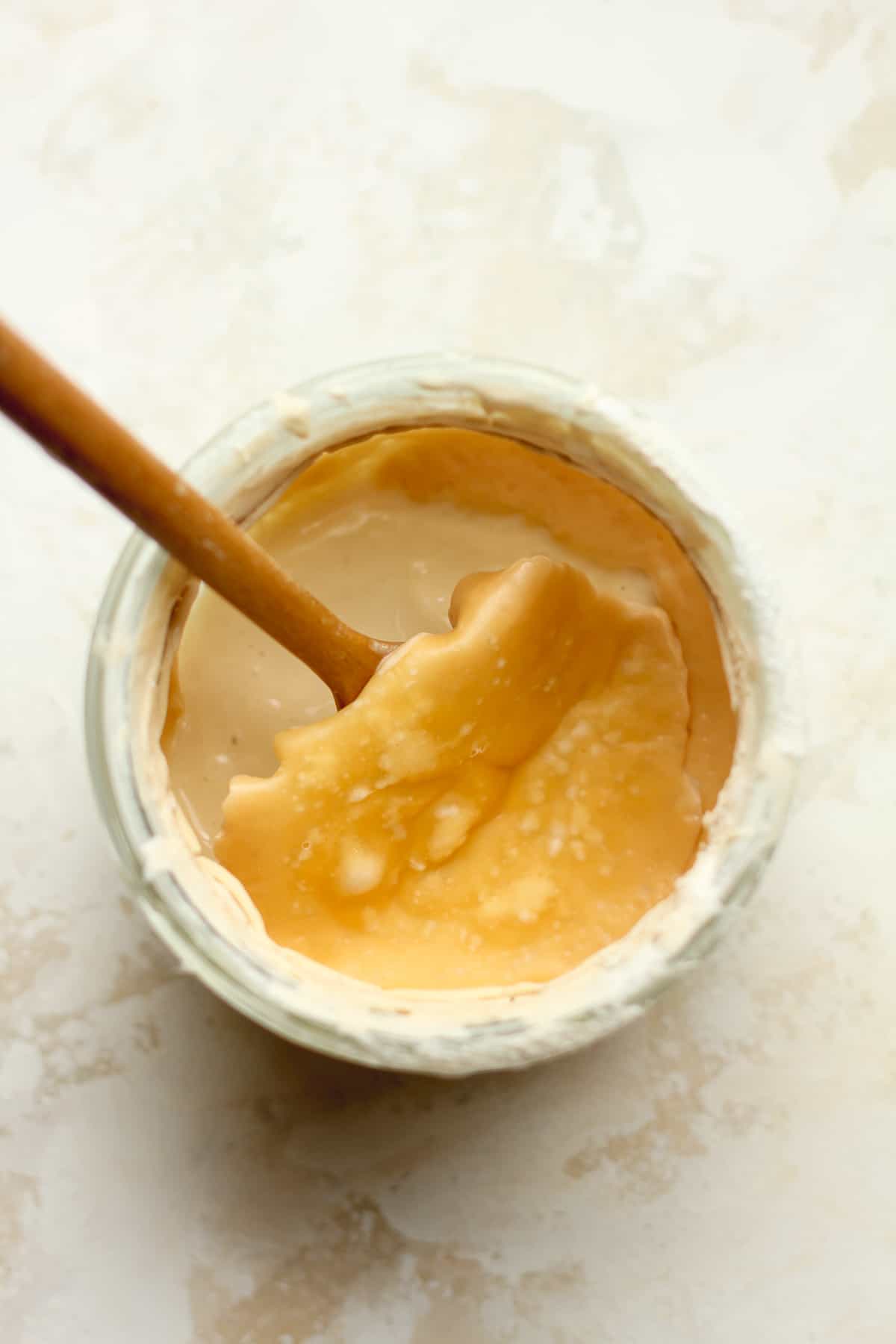 A jar with a wooden spoon lifting the brown layer off the starter to discard.