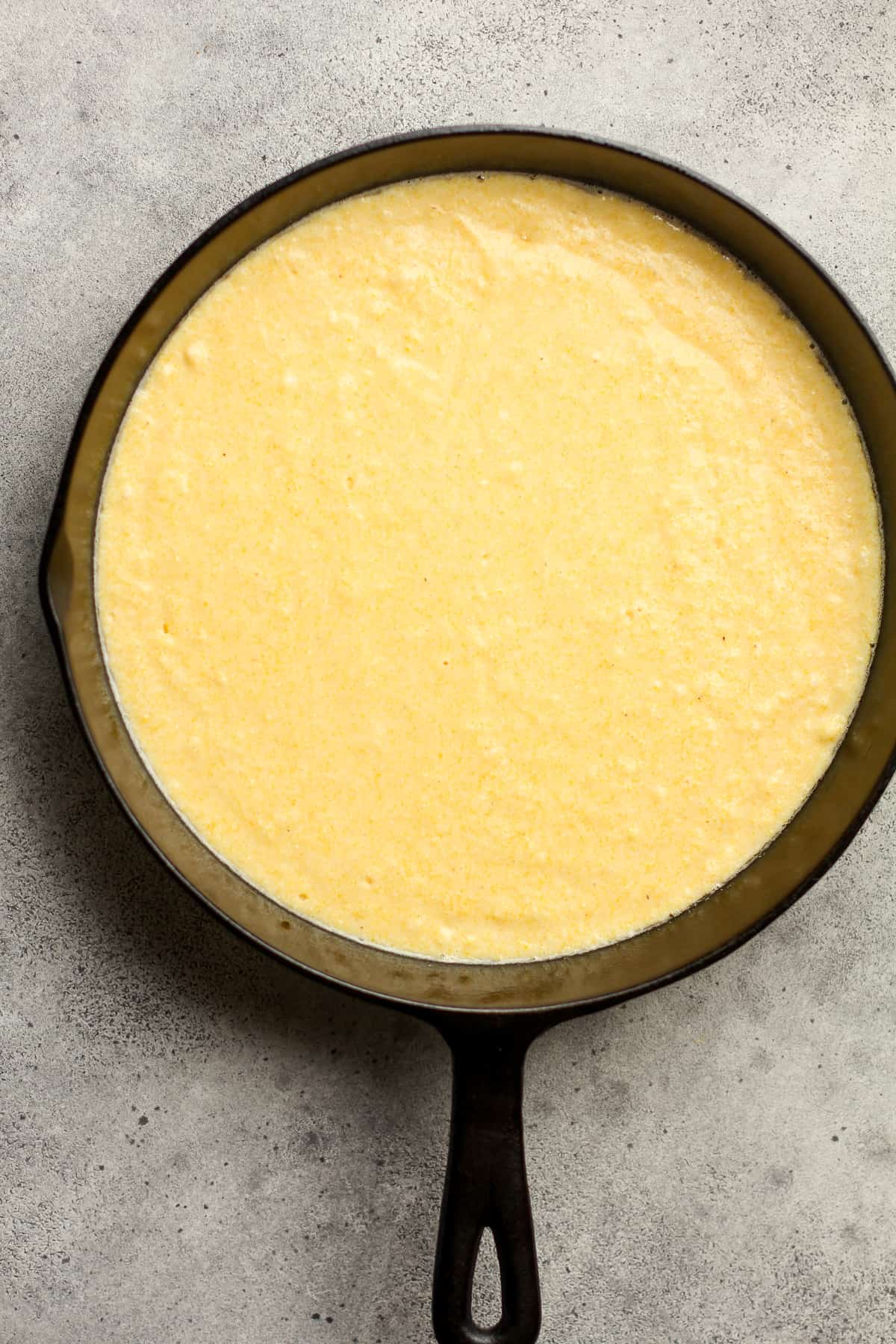 A skillet of cornbread batter on a gray background.