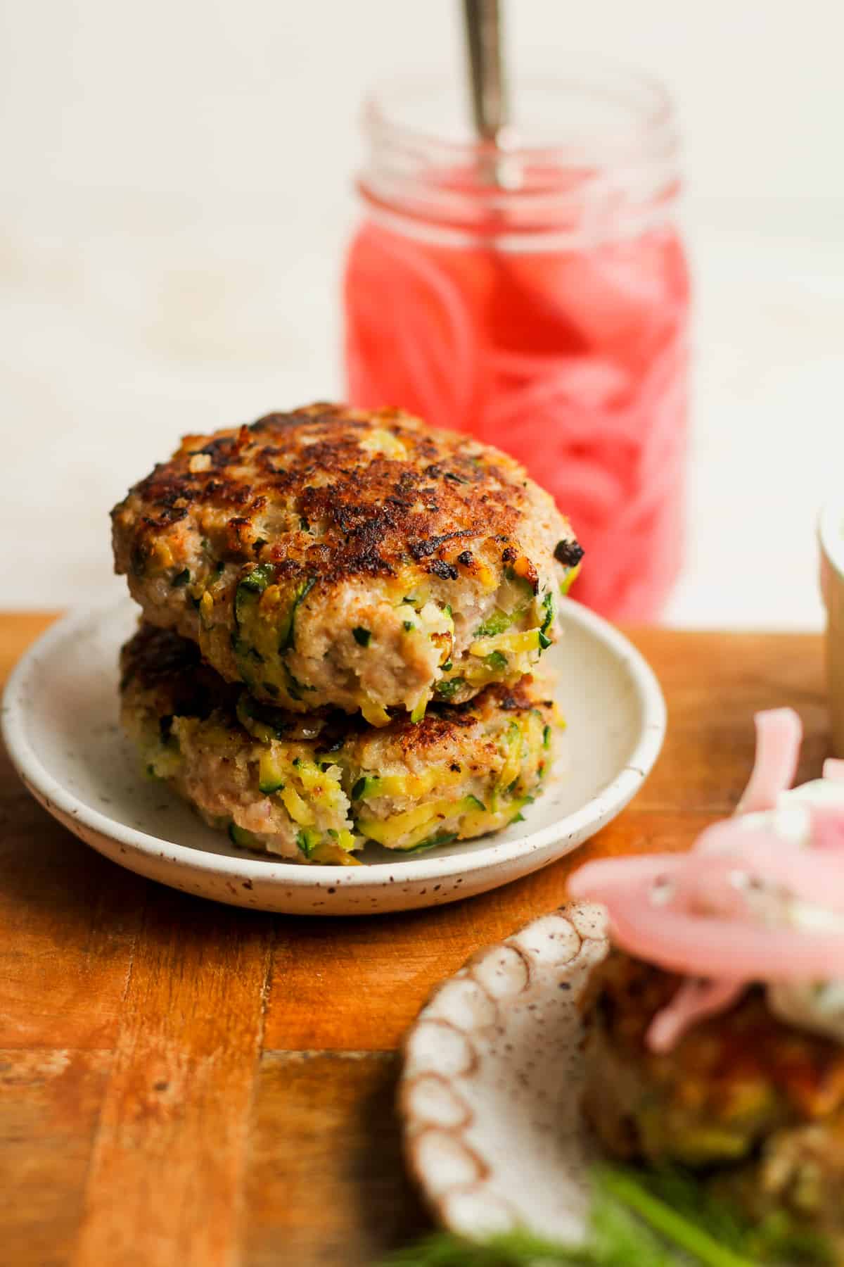 Side view of two thick turkey zucchini burgers with a jar of red pickled onions.