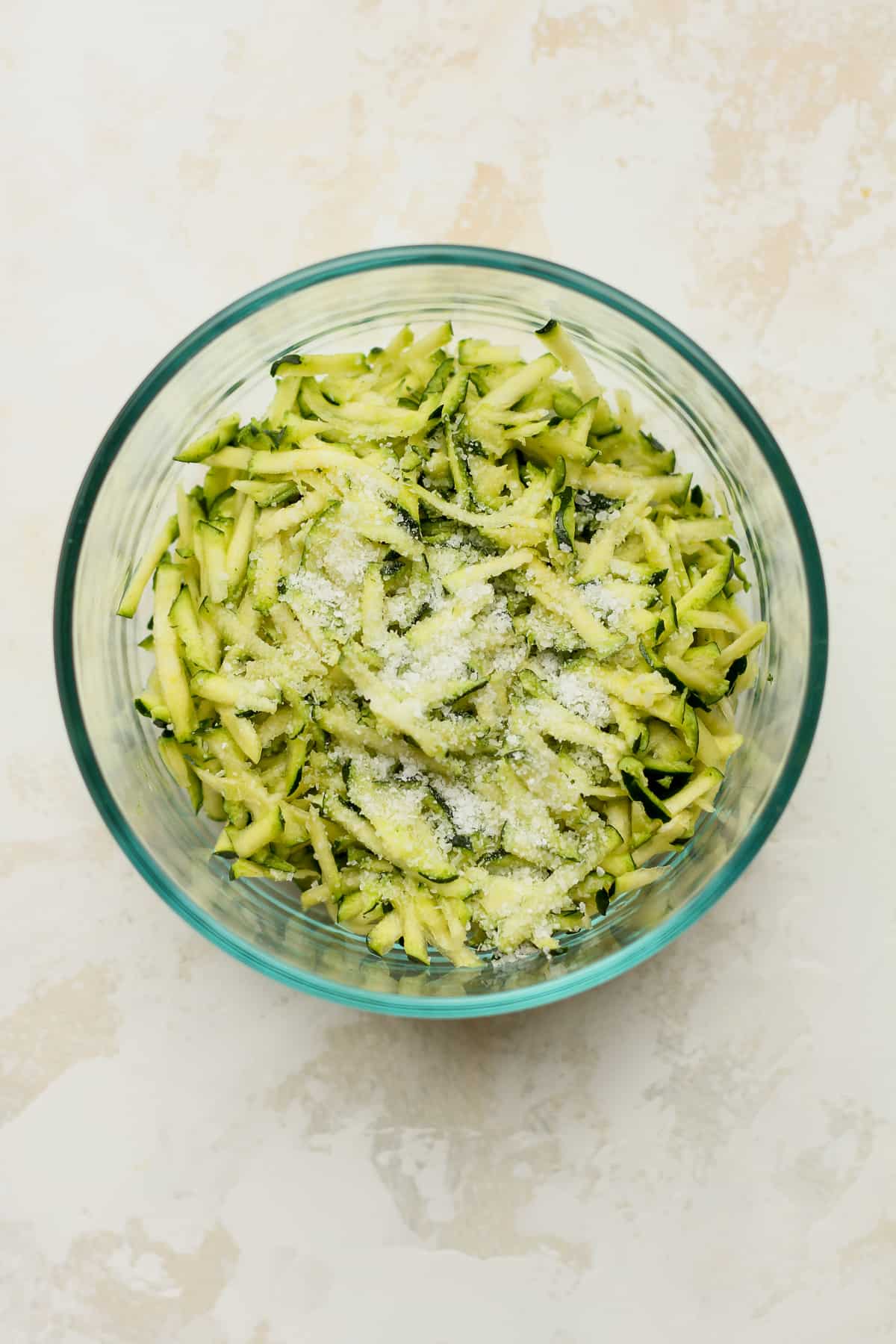 A bowl of shredded zucchini with salt on top.