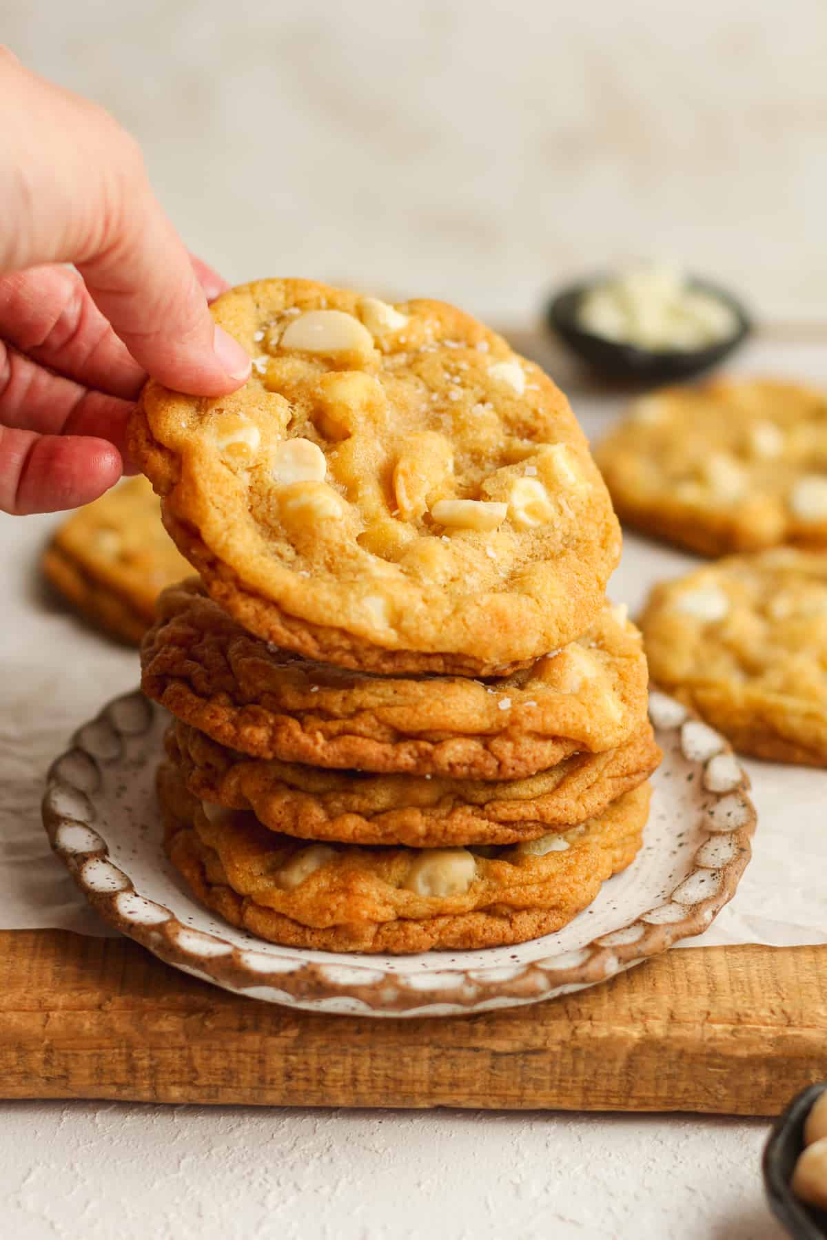 My hand reaching for a macadamia nut cookie on top of a stack of cookies.