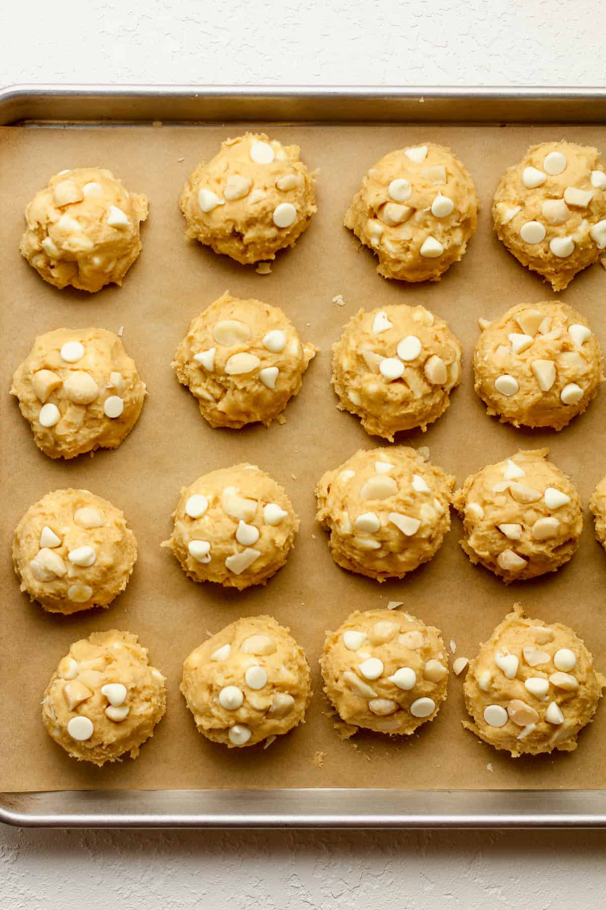 A baking sheet with cookie balls with white chips and macadamia nuts.
