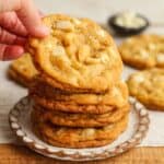 A hand reaching for a white chocolate macadamia nut cookies.