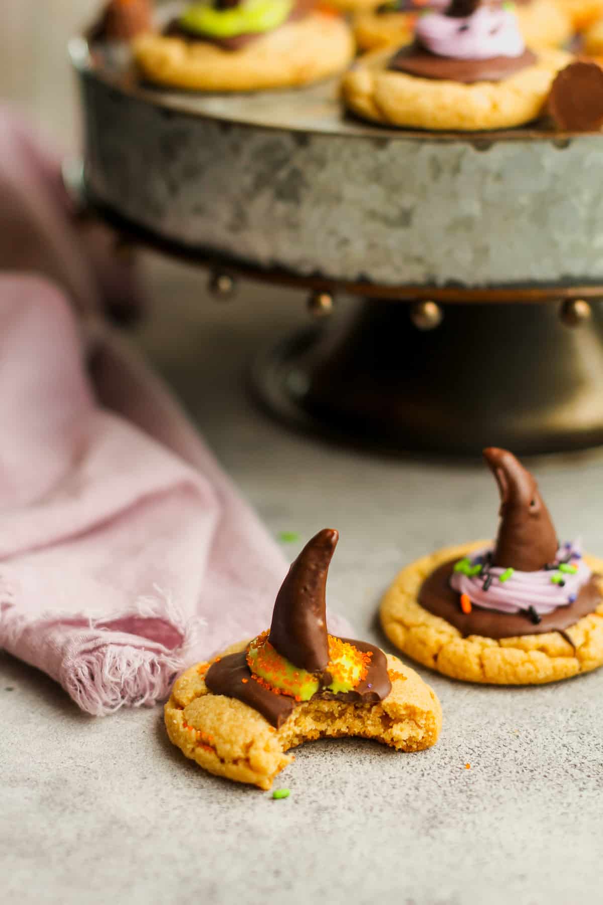 A witch hat cookie with a bite out and a tray of cookies in the background.