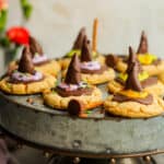 A silver cake plate of peanut butter witch hat cookies with colorful sashes.