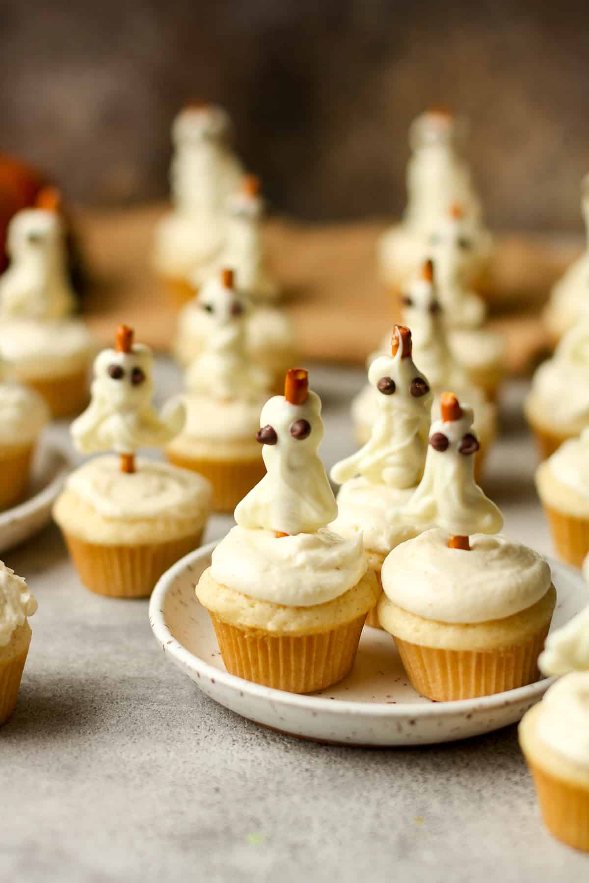 Side view of several vanilla bean cupcakes with buttercream frosting and pretzel ghosts.