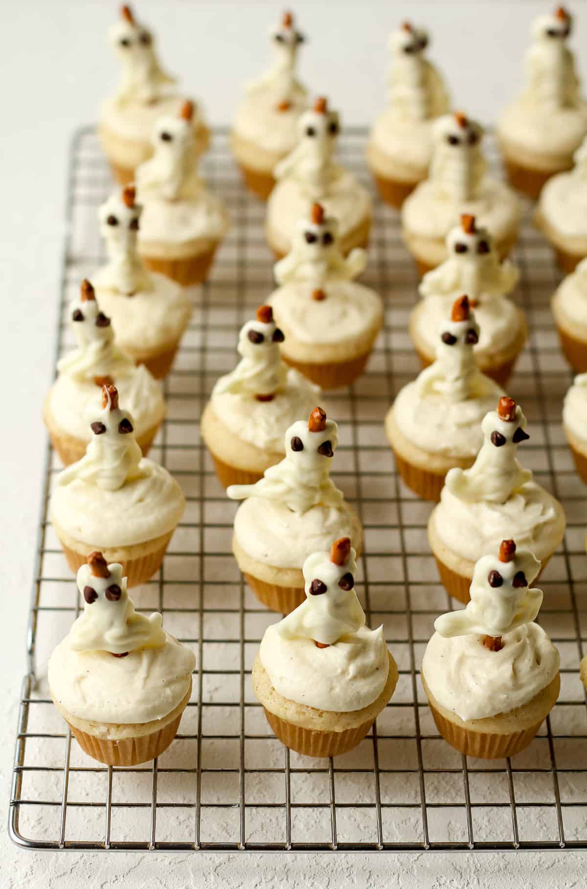 A wire rack of just made Halloween ghost cupcakes.