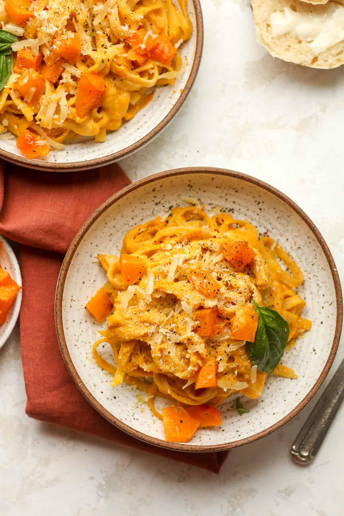 Two bowls of roasted butternut squash pasta with a dark orange napkin.