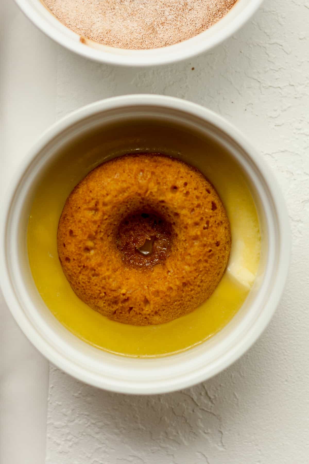 A pumpkin donut in a bowl of melted butter.