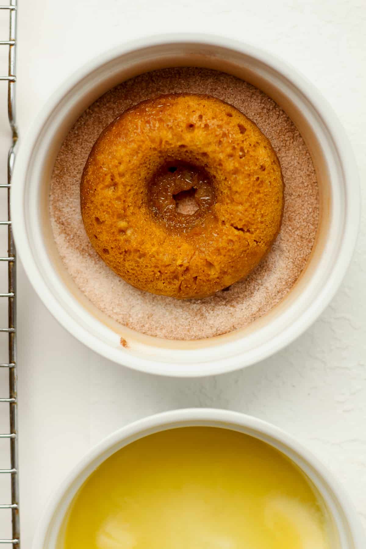 A pumpkin donut in a bowl of cinnamon sugar.