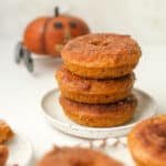 A small plate with three stacked pumpkin donuts with cinnamon sugar topping.