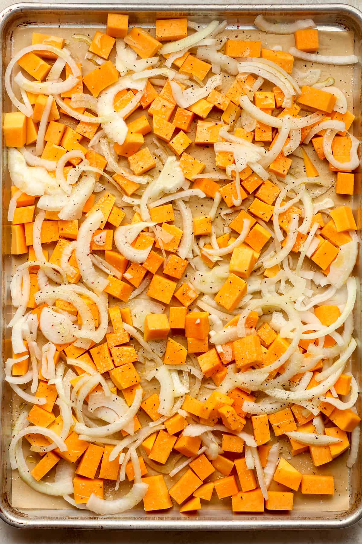 A sheet pan of chopped butternut squash and sliced onions.