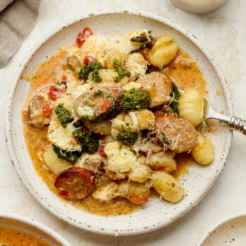 A plate of sausage and gnocchi with cheese and pesto.