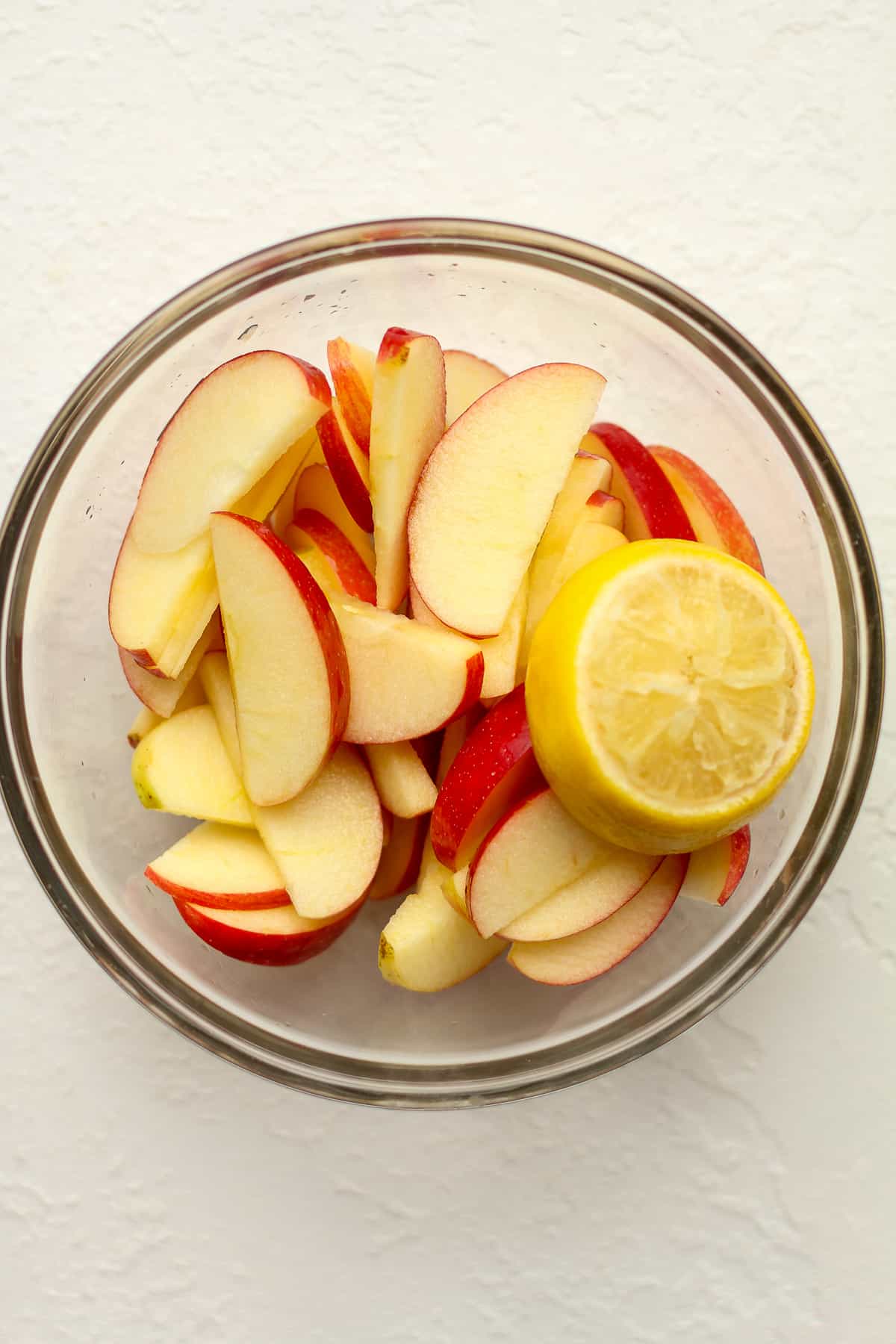 A glass bowl of the apple slices with a half of a lemon on top.