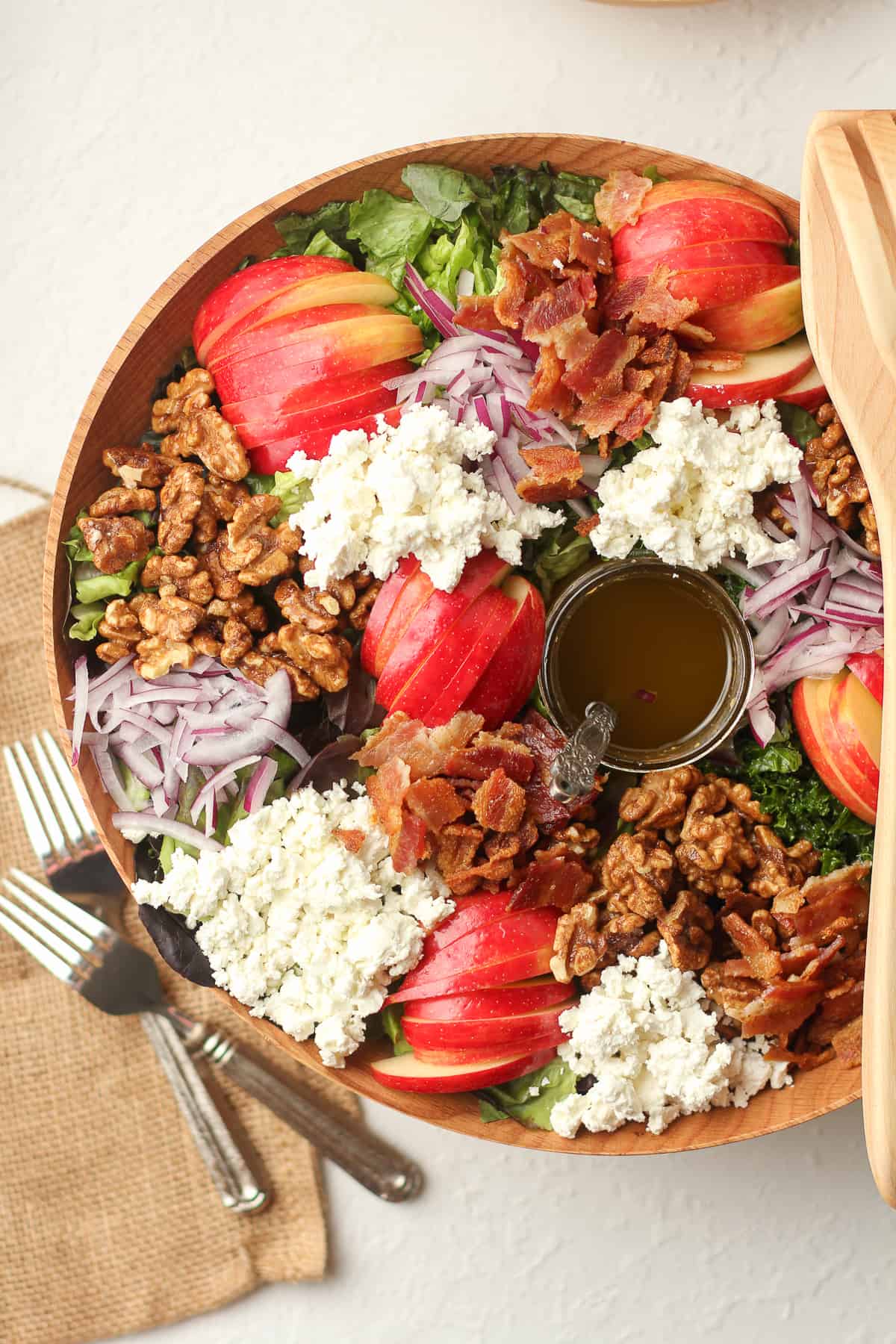A wooden bowl of the fall harvest salad with apple slices, bacon, candied walnuts, and goat cheese.