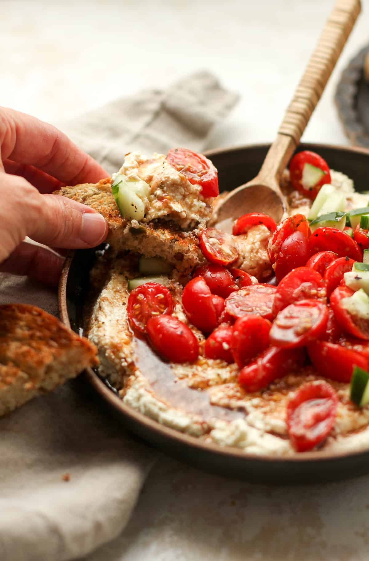 My hand on a toast with feta dip and marinated tomatoes.