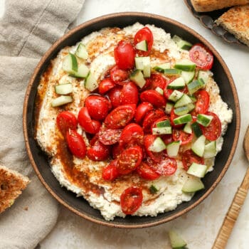 A bowl of feta dip with tomatoes and cucumbers.