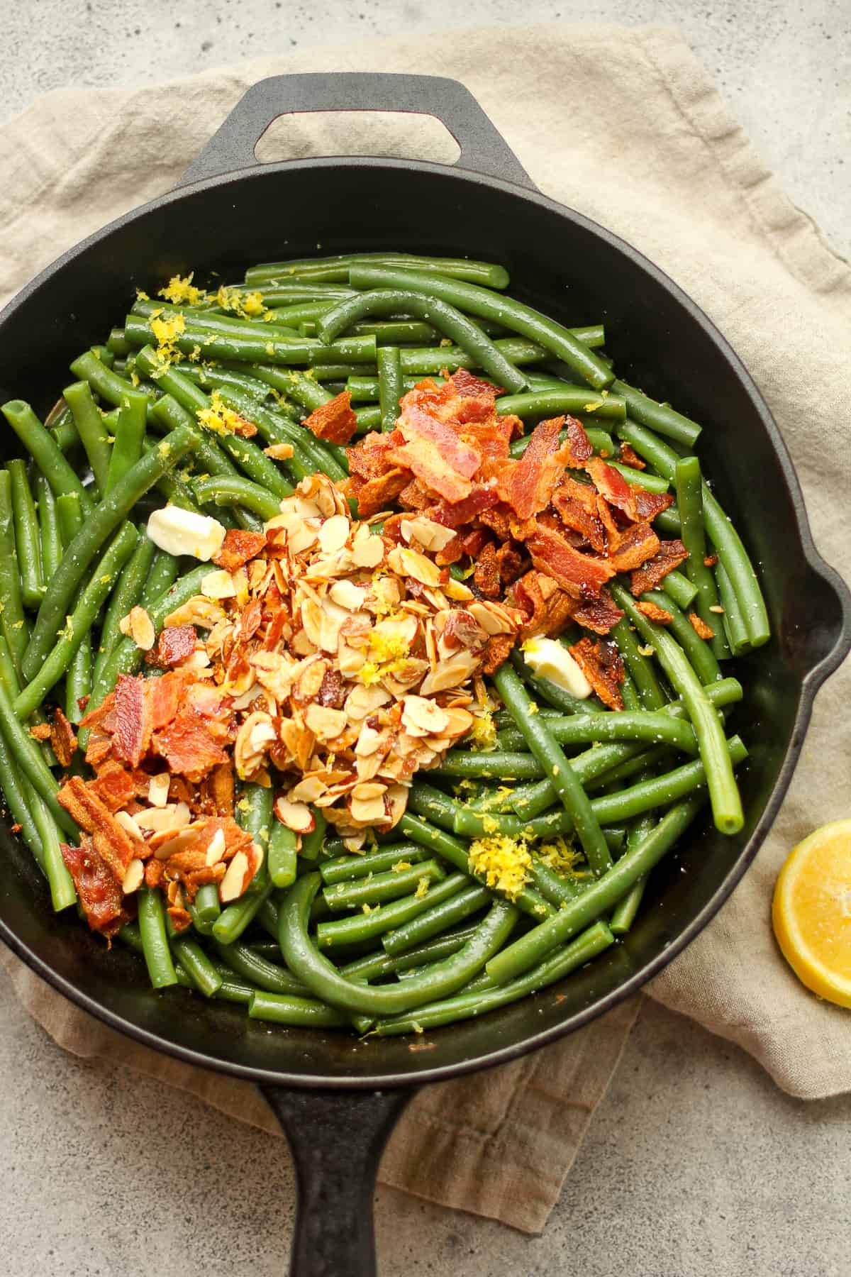 The green beans in a skillet with bacon and almonds on top.