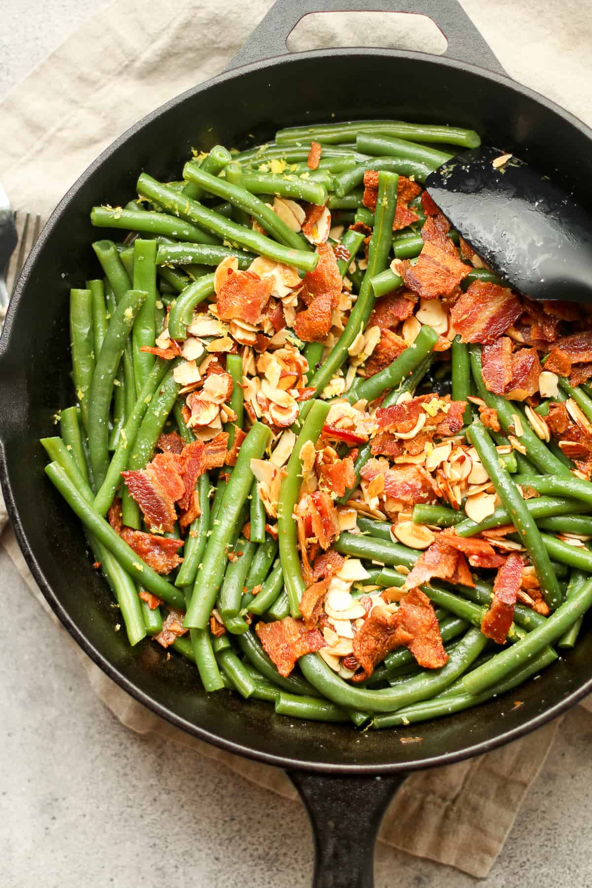Overhead view of a skillet of green bean almandine with bacon.