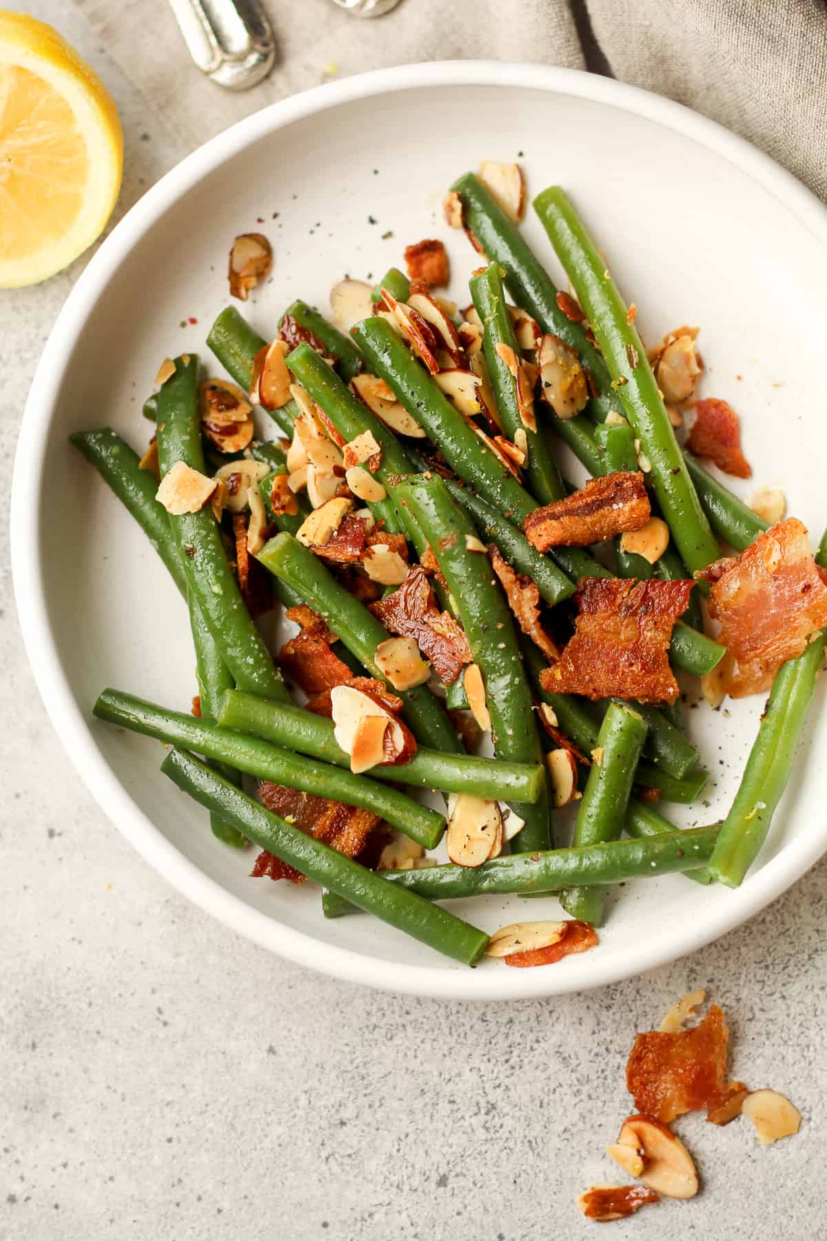 A serving plate of the green bean almandine with bacon on top.