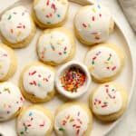 A large plate of lemon ricotta cookies with a small bowl of sprinkles.