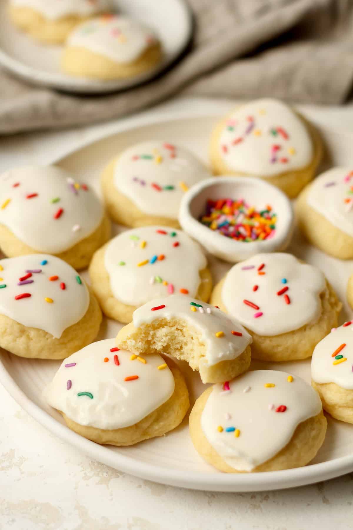Side view of a large plate of lemon ricotta cookies, one with a bite out.
