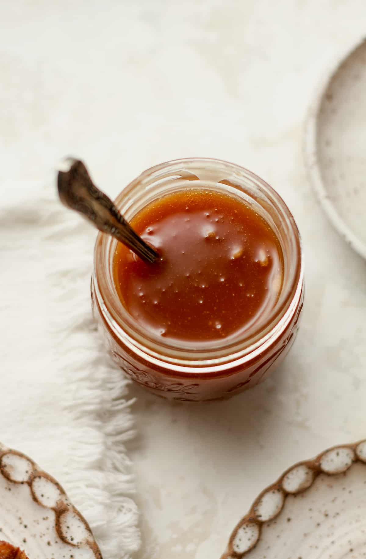 Overhead view of a small jar of caramel sauce with a spoon.