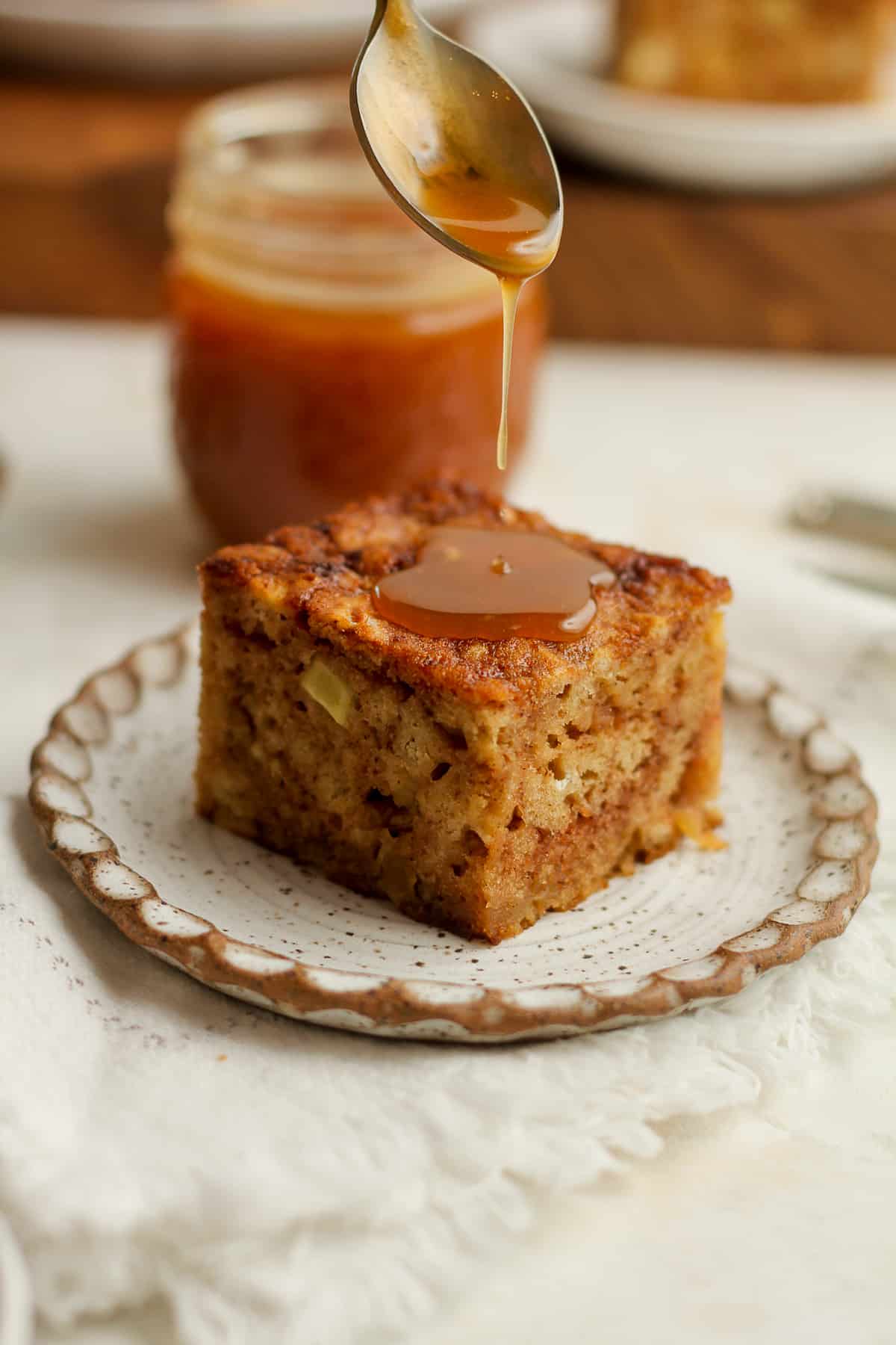 Side view of a slice of applesauce cake with a spoonful of caramel sauce drizzling on top.