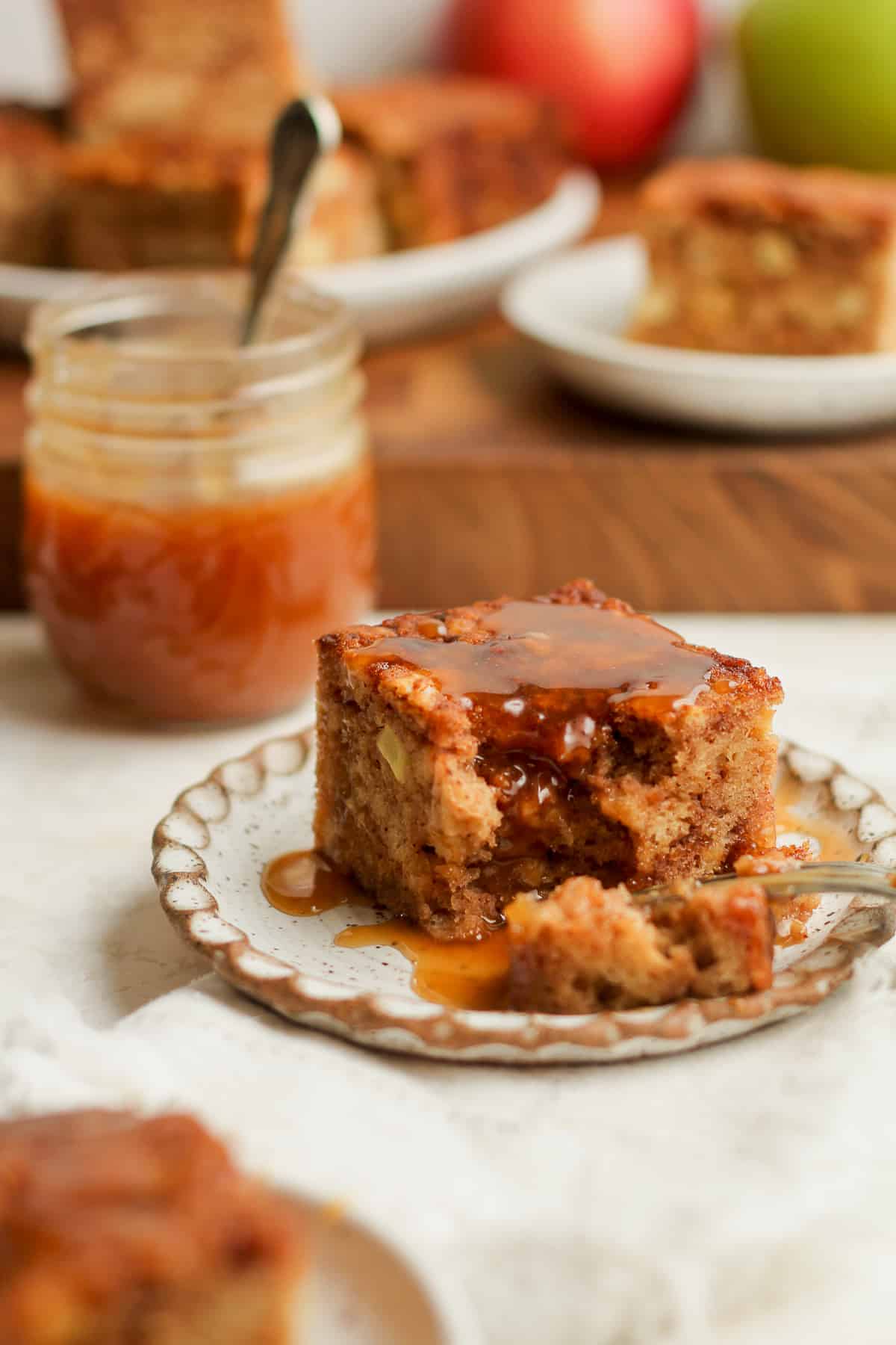 Side view of a slice of applesauce cake with caramel sauce, and a jar of caramel in the background.