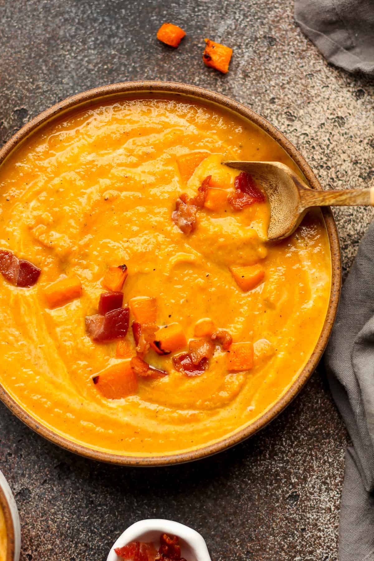 A shallow bowl of butternut squash soup with cubes of squash and bacon.