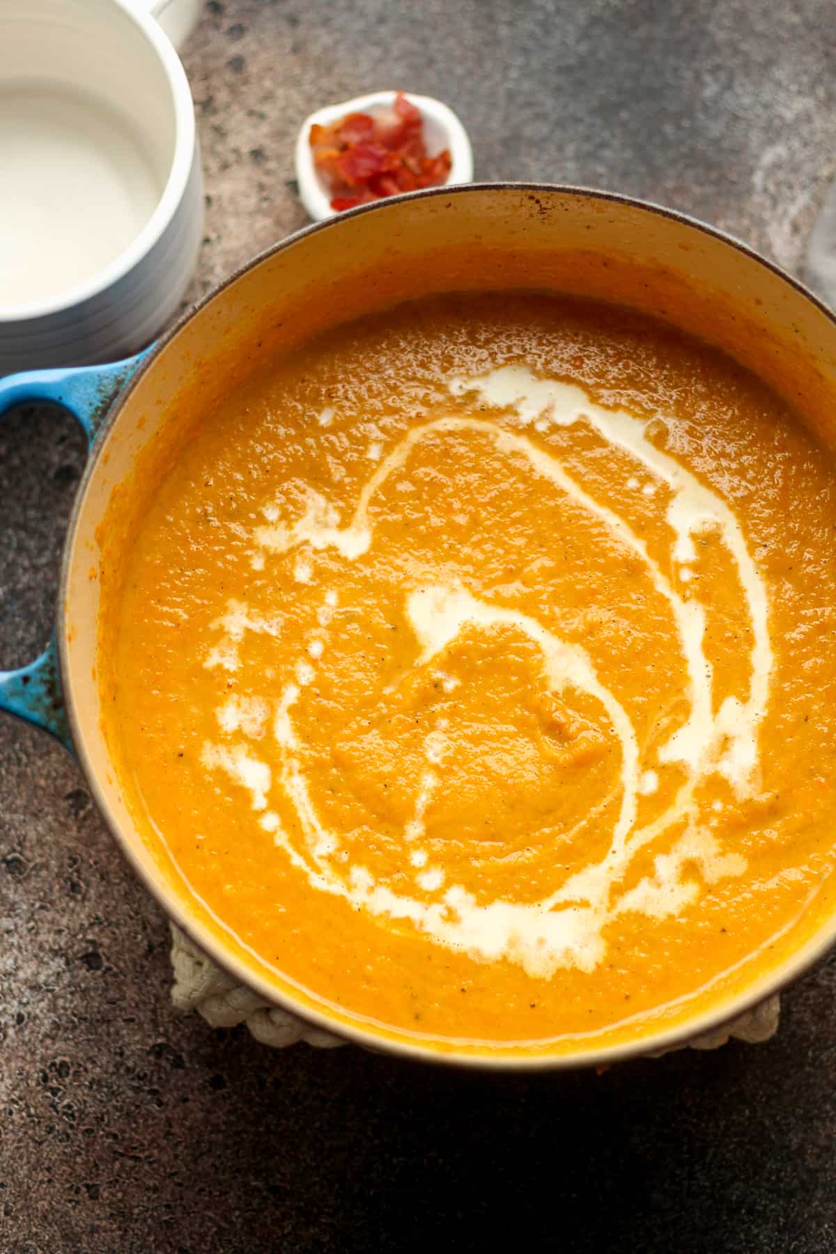 A pot of pureed butternut squash soup with a drizzle of half and half.