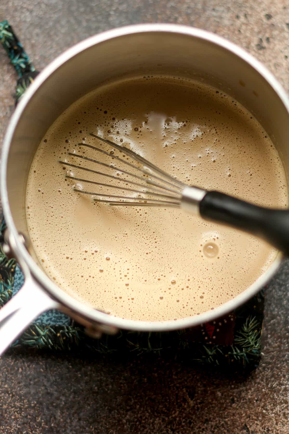 A small pan of eggnog lattes with a whisk.