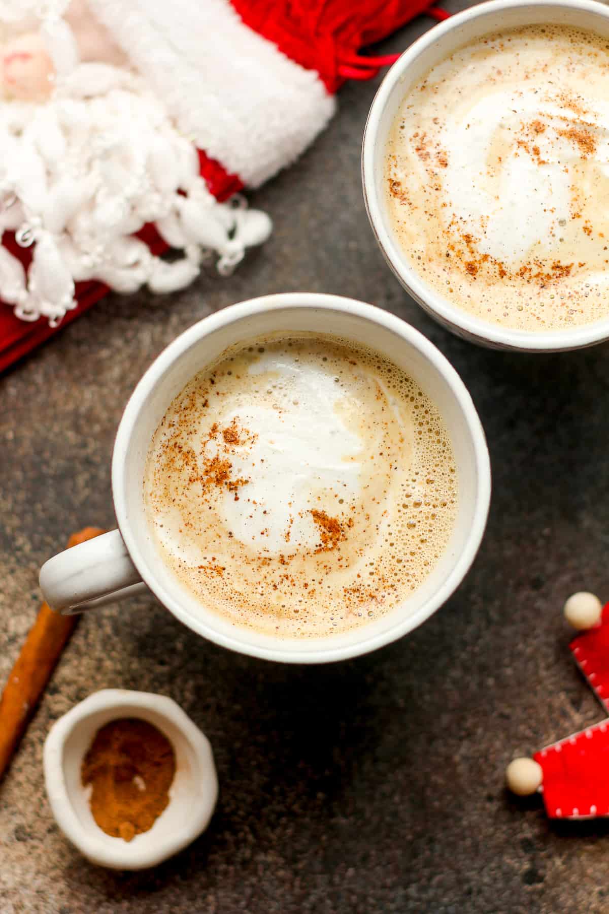 Overhead shot of two mugs of eggnog lattes with nutmeg sprinkles.