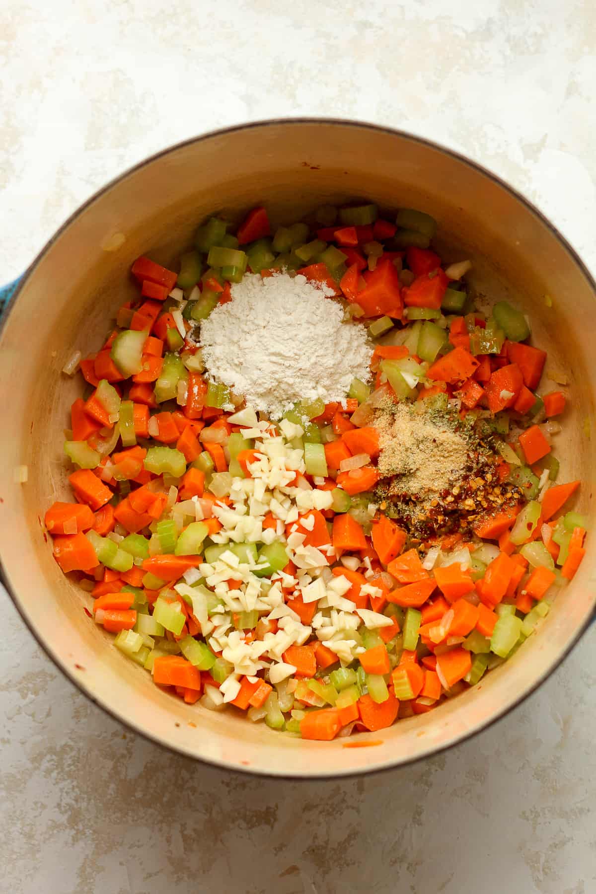 A pot of the diced veggies with minced garlic, seasonings, and flour on top.