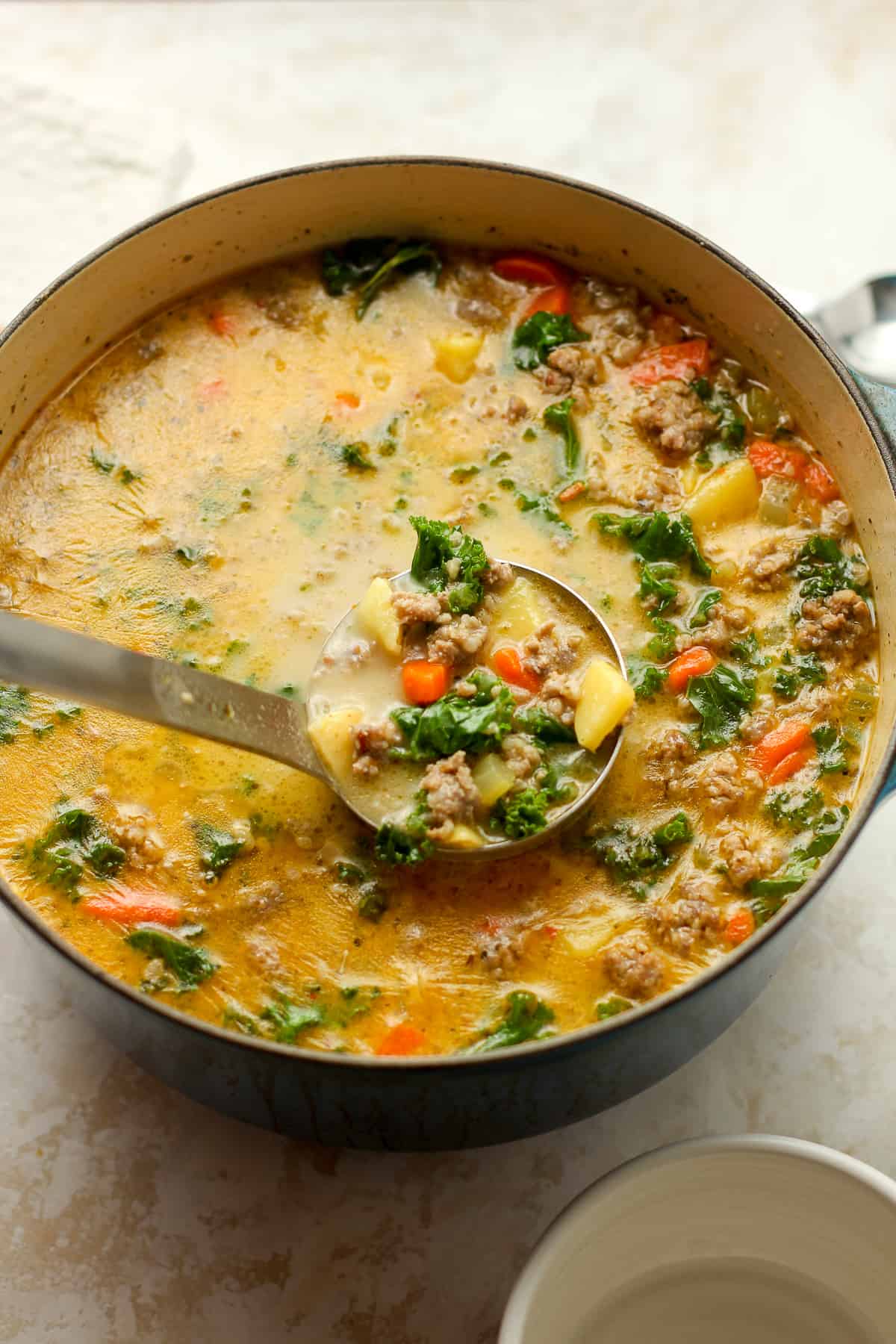 A pot of healthy Zuppa Toscana with a soup ladle pulling some upward.