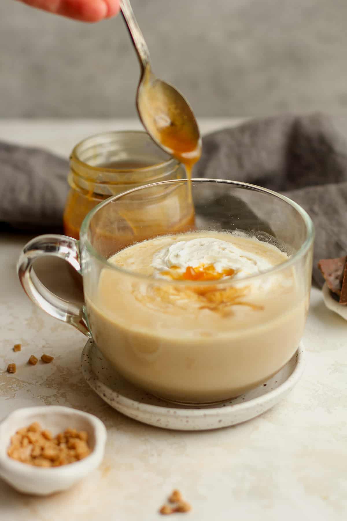 Side view of a mug of caramel latte with a spoon of caramel over top.