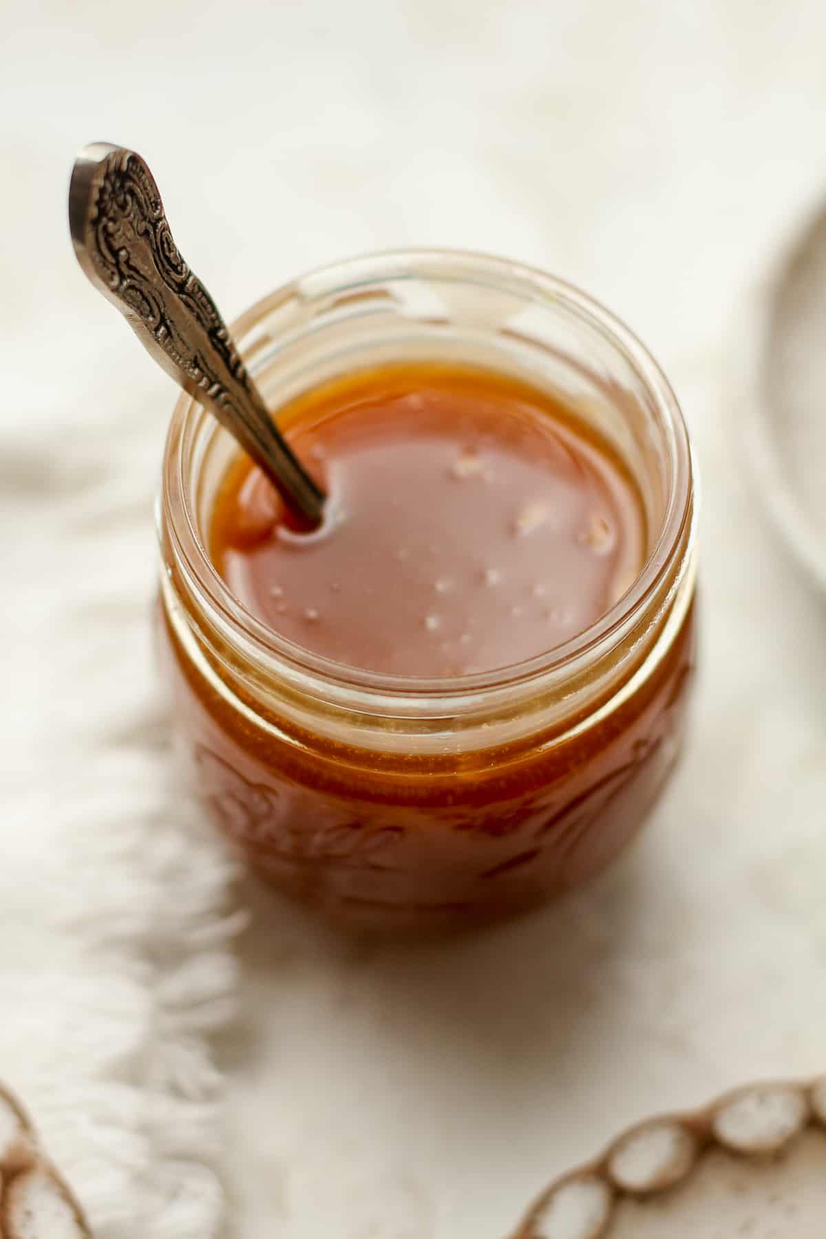 A jar of homemade caramel sauce with a spoon.