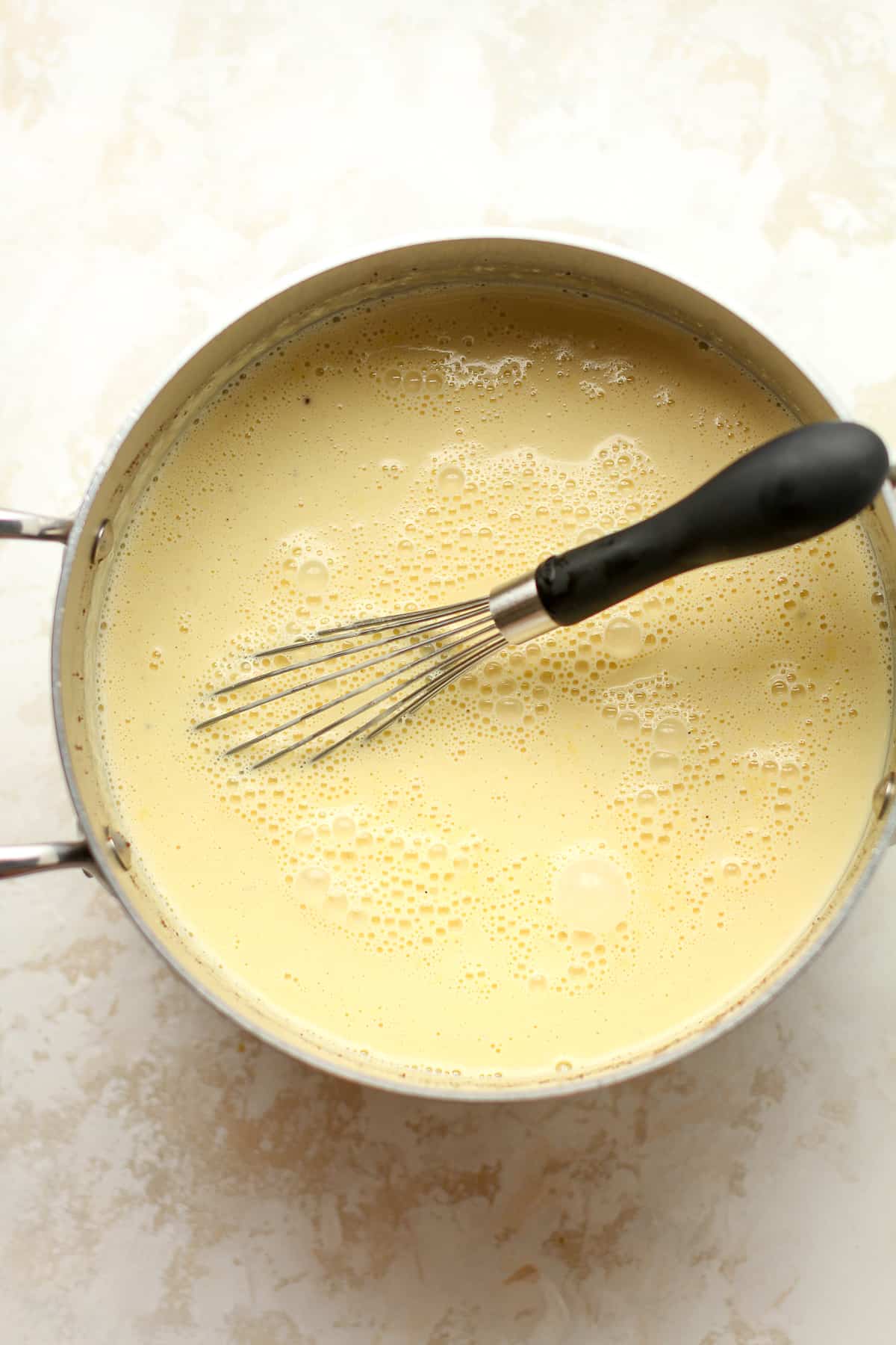 A pan of just made homemade eggnog with a whisk.